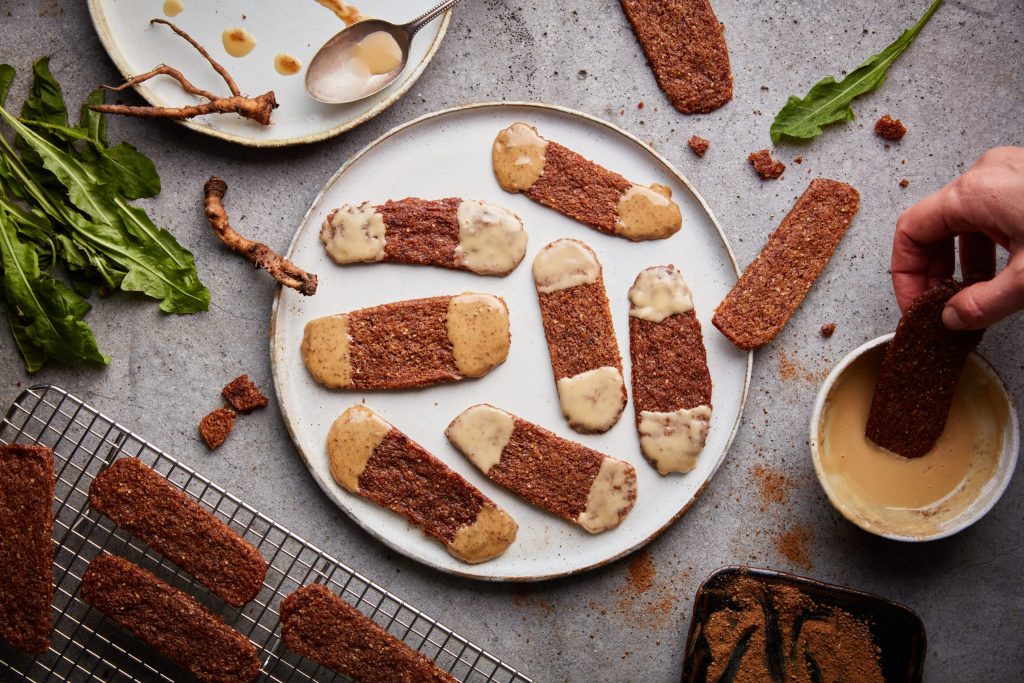 Roasted dandelion and almond thins being dipped into homemade icing