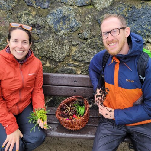 Couple sitting on a bench at Perranuthnoe with a foraging basket with leaves, berries and wild spices in