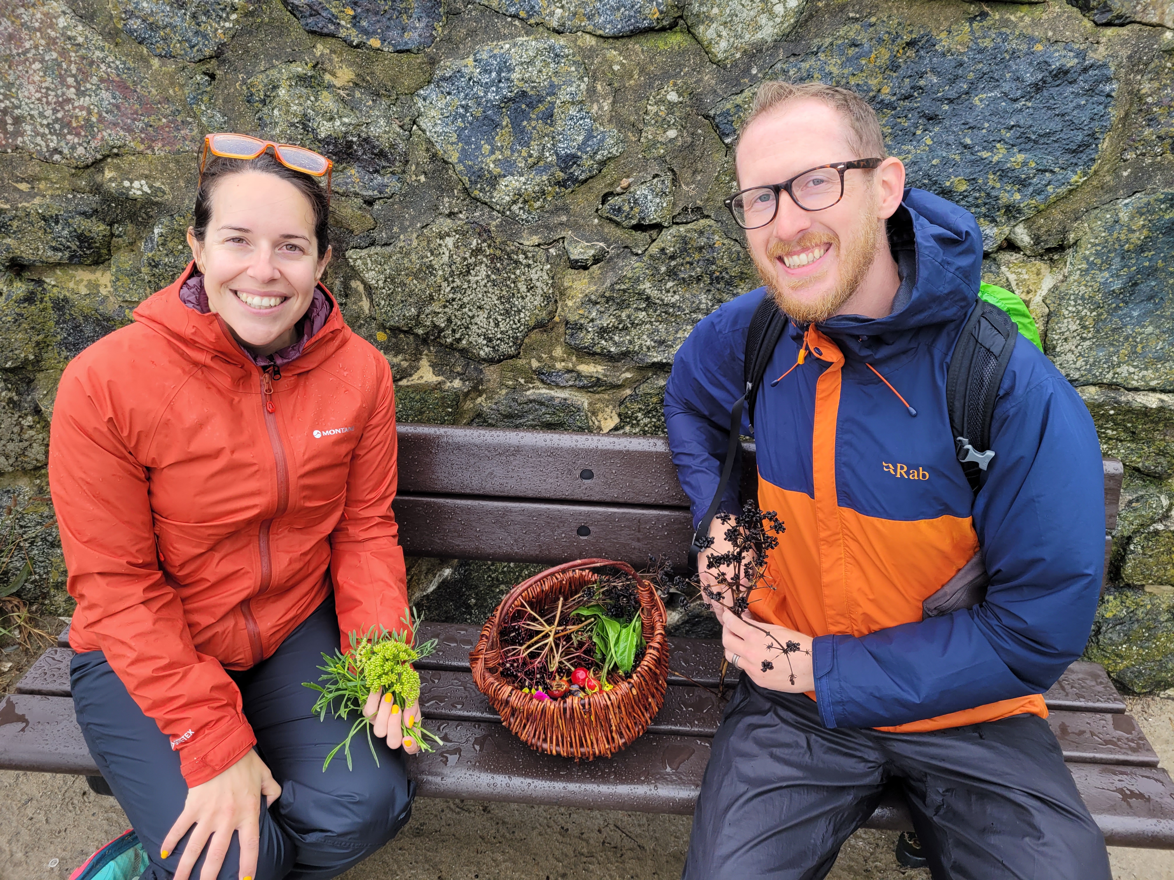 Couple sitting on a bench at Perranuthnoe with a foraging basket with leaves, berries and wild spices in