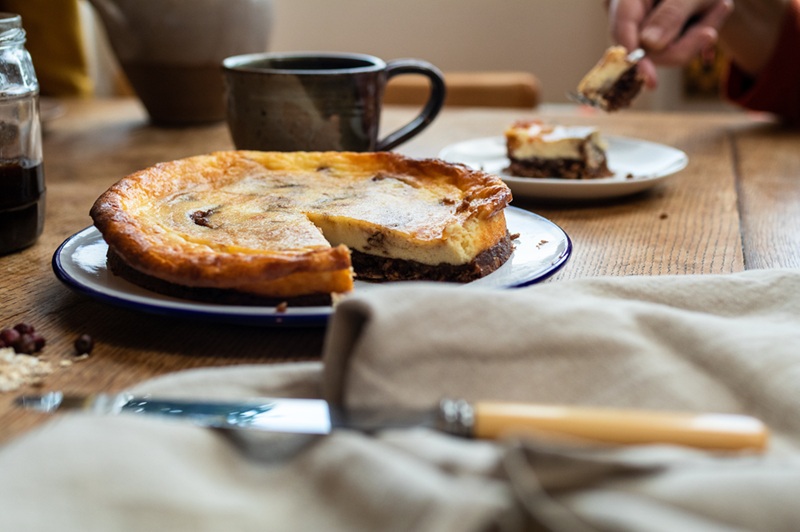 A baked cheesecake with haw berry jam, a cup of tea and half eaten slice on a wooden kitchen table