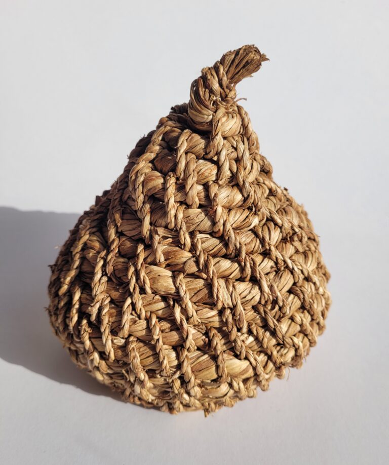 A 3-dimensional object, shaped like a fruit or bulb, woven from dried and golden daffodil stems