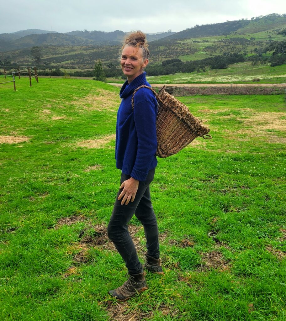 Forager Rachel Lambert standing in a green field with a Kishie on her back