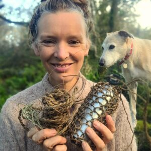 Forager Rachel Lambert in a wood holding plant fibres made into string, rope and a bag
