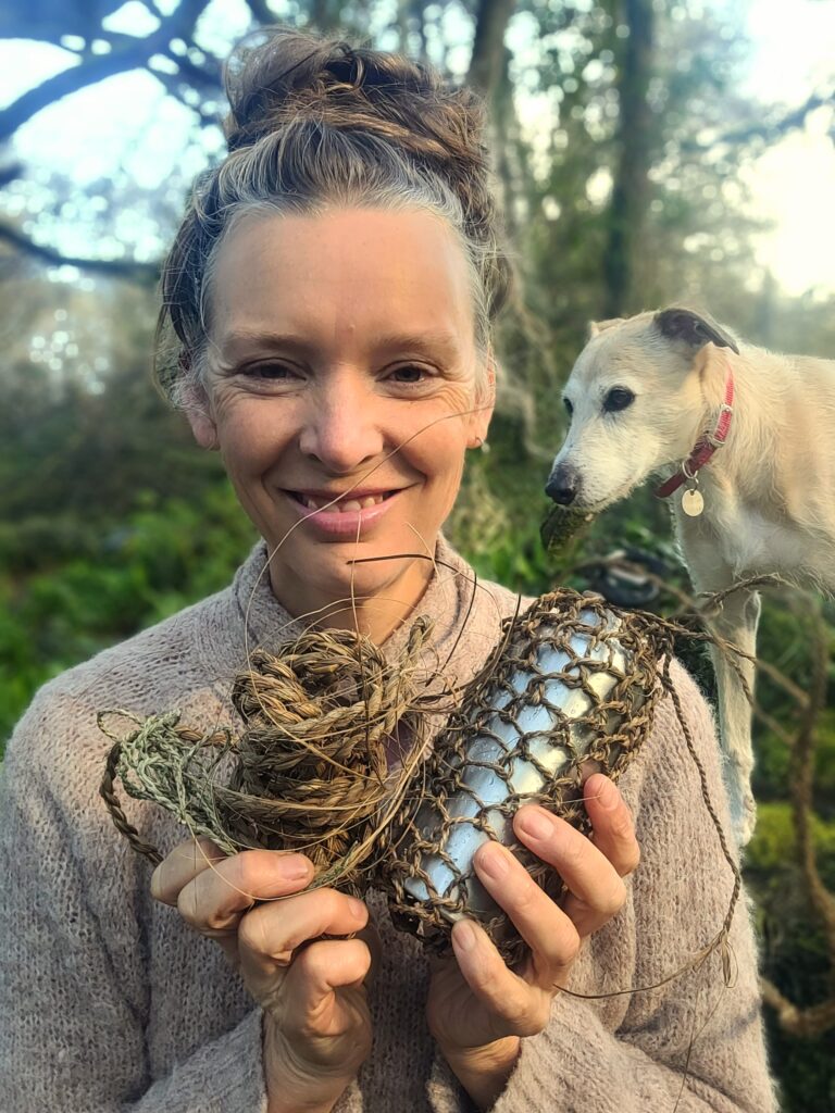 Forager Rachel Lambert in a wood holding plant fibres made into string, rope and a bag