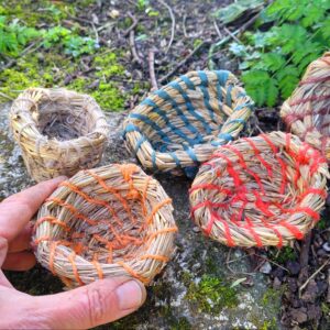 5 straw coil pots on a rock with a hand holding one