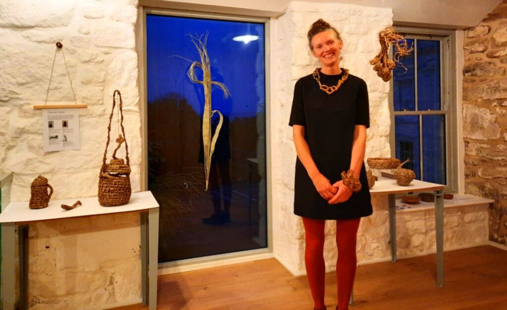 Artist and artisan maker Rachel Lambert standing in her exhibtion 'Weeds of Penzance' in The Gardeners' House