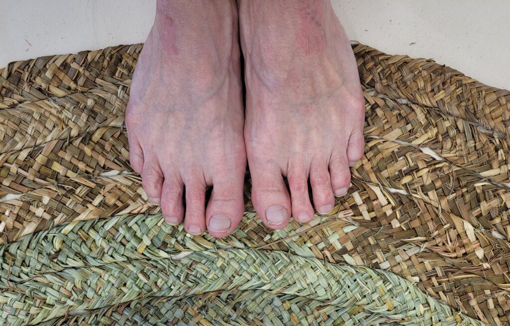 Two bare feet on a hand woven mat made from plants growing in Cornwall, UK