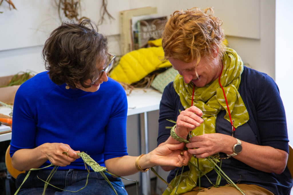 Two women talking and laughing while holding their creations from local plants