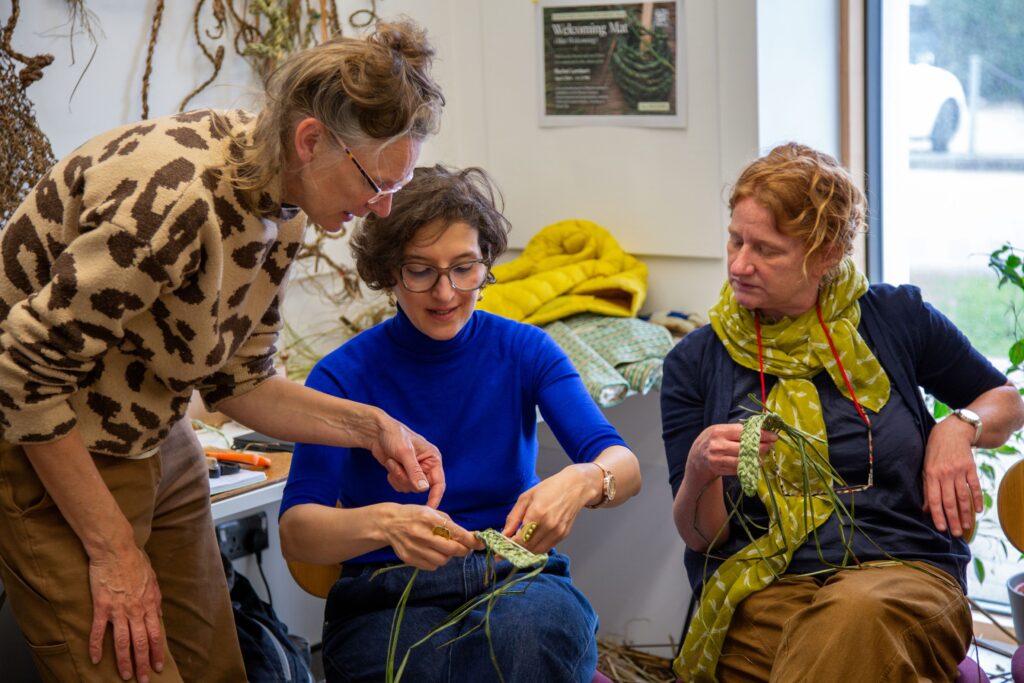 Rachel Lambert guiding two women on how to weaving sedges to make a basket