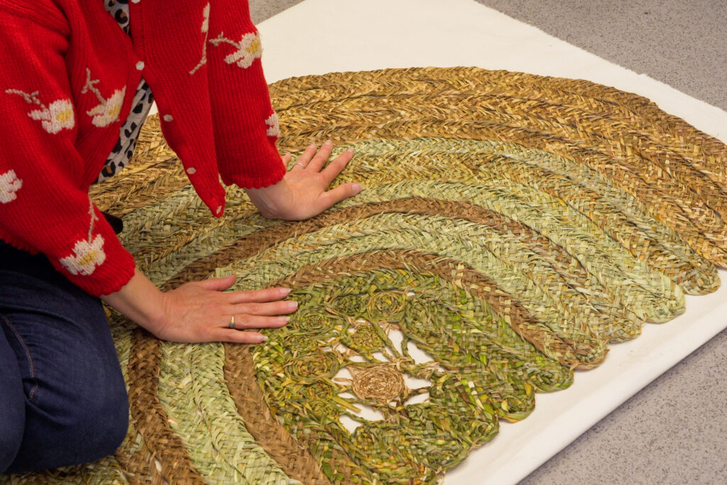 A woman sitting on and touching the Welcoming Mat which is made from 100% foraged plants